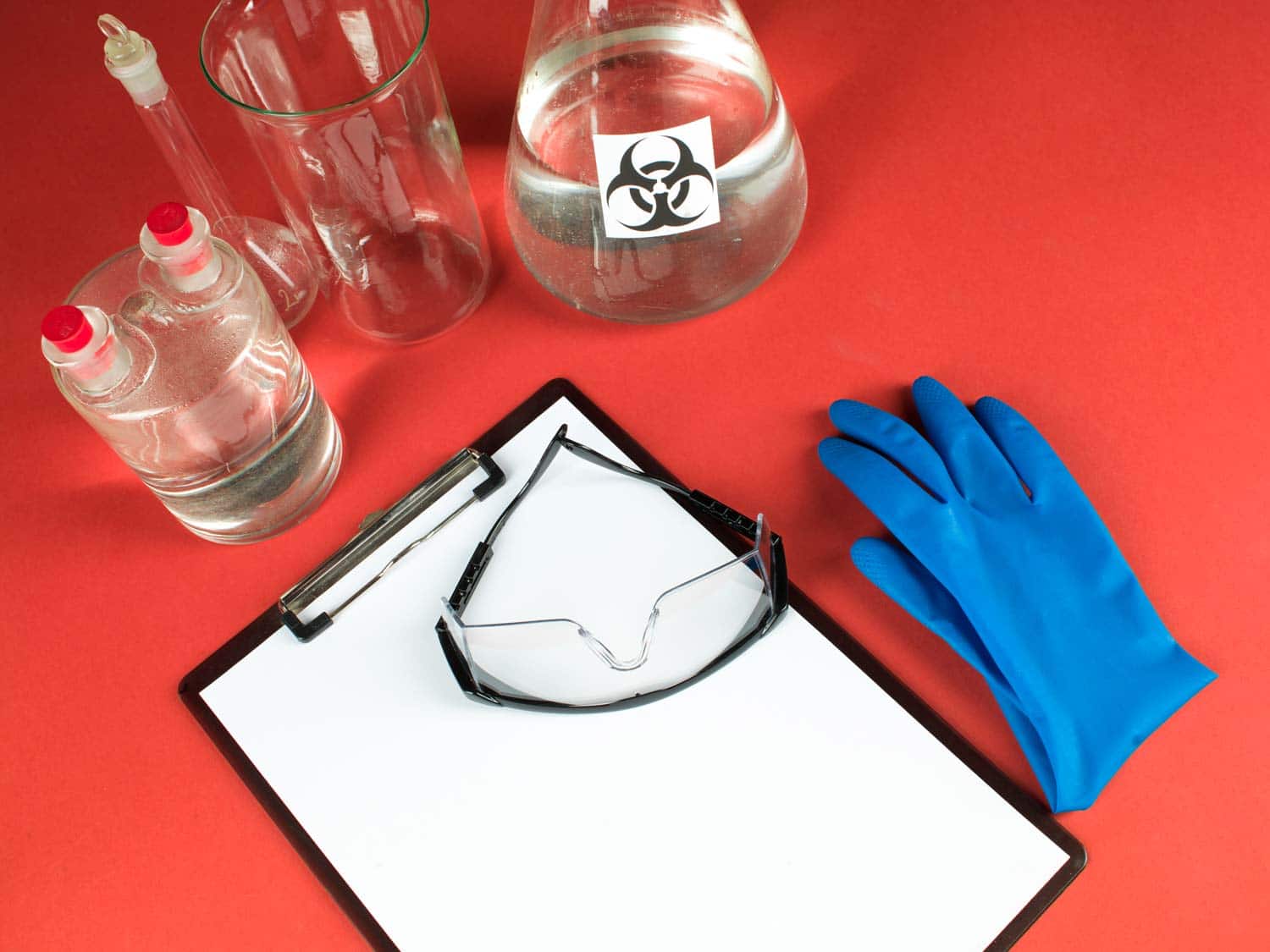 Laboratory glassware, protective gloves and a clipboard on a science workbench